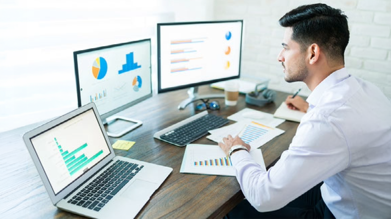 A business professional reviewing charts and data on multiple screens for market research for new business planning and analysis.